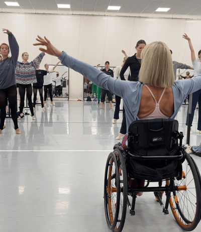 Suzie sits in her wheelchair teaching a group of dancers in a studio.